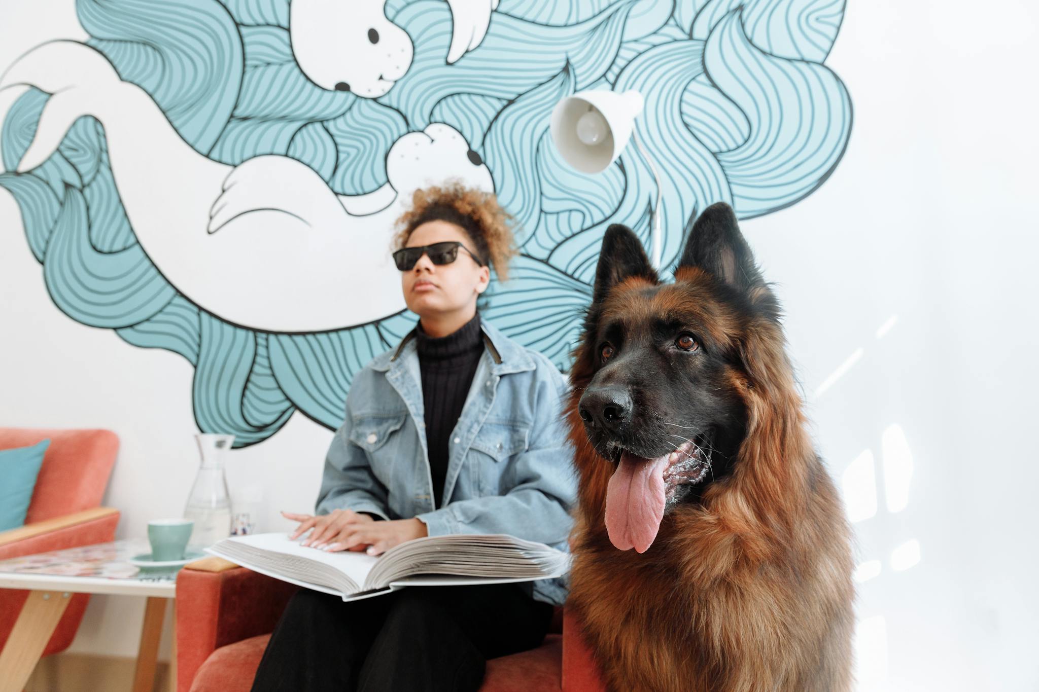Blind woman reading a braille book with her German Shepherd guide dog indoors.