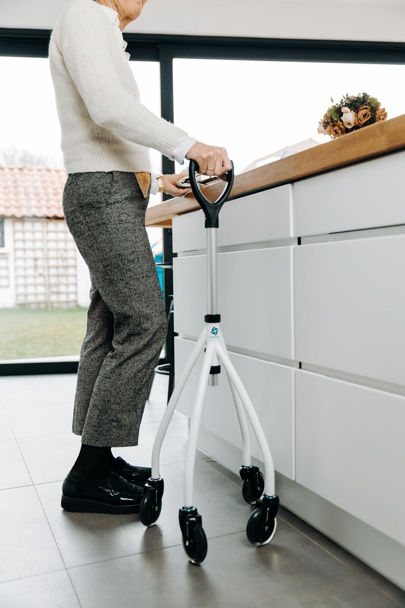 Elderly person using a modern walker in a spacious, well-lit kitchen environment.